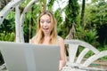 Young happy woman resting on swing and using laptop, palms in background. Royalty Free Stock Photo