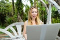 Young happy woman resting on swing and using laptop, palms in background. Royalty Free Stock Photo