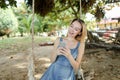 Young happy woman riding swing and using smatrphone, sand and tree in background. Royalty Free Stock Photo