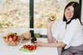 Young happy woman showing half of perfectly ripe avocado in hand and smiling on background of fresh fruits and vegetables in Royalty Free Stock Photo