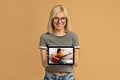 Young happy woman showing tablet pc with online guitar lesson on screen over beige studio background Royalty Free Stock Photo