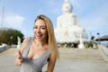 Young happy woman showing thumbs up, white Buddha statue in Phuket in background.