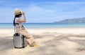Young happy woman sit on travel suitcase on the beach in summer. Travel woman looks at the sea. Women sitting and relax with beach Royalty Free Stock Photo