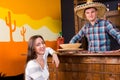 Young happy woman sitting at the bar counter next to the bartender wearing sombrero