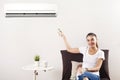 Young Happy Woman Sitting On Couch Operating Air Conditioner With Remote Control At Home Royalty Free Stock Photo