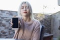 Young happy woman sitting on home terrace showing smartphone