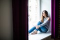 Young happy woman sitting on a window-sill at home and looking outside Royalty Free Stock Photo