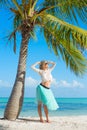 Young happy woman standing on beach under palm tree