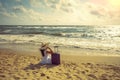 Young happy woman in a straw hat with a travel suitcase sits on the beach Royalty Free Stock Photo