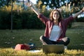 Young happy woman student sitting on the grass in the park in front of laptop with hands raised up Royalty Free Stock Photo