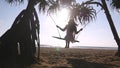 Young happy woman in swimsuit and shirt relaxing at swing at tropical ocean beach. Beautiful girl sitting on swing and Royalty Free Stock Photo