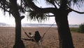 Young happy woman in swimsuit and shirt relaxing at swing at tropical ocean beach. Beautiful girl sitting on swing and Royalty Free Stock Photo