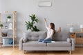 Young woman switching on air conditioner sitting on couch Royalty Free Stock Photo