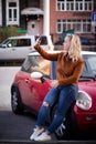 Young happy woman taking new photos on smartphone on the street. Girl doing selfies for social nets on the road with Royalty Free Stock Photo