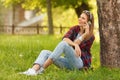 Young happy woman talking on cell phone sitting on grass in summer city park. Beautiful modern girl with a smartphone, outdoor Royalty Free Stock Photo