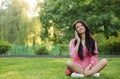 Young happy woman talking on cell phone sitting on grass in summer city park Royalty Free Stock Photo