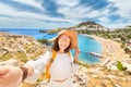 Happy woman tourist taking selfie photo on her smartphone with view on a sandy beach and old town. Vacaction and travel Royalty Free Stock Photo