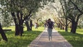 Young happy woman tourist is walking alone in spring sunny city park with blooming apple trees on background. Concept of