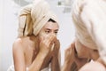 Young happy woman in towel making facial massage with organic face scrub and looking at mirror in stylish bathroom. Girl applying Royalty Free Stock Photo