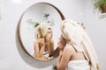 Young happy woman in towel making facial massage with organic face scrub and looking at mirror in stylish bathroom. Girl applying Royalty Free Stock Photo