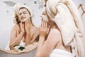 Young happy woman in towel making facial massage with organic face scrub and looking at mirror in stylish bathroom. Girl applying Royalty Free Stock Photo