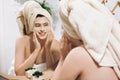 Young happy woman in towel making facial massage with organic face scrub and looking at mirror in stylish bathroom. Girl applying Royalty Free Stock Photo