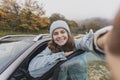 Young happy woman traveling by car taking selfie while standing on country road, in autumn Royalty Free Stock Photo