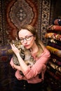 Young happy woman trying to kiss funny turkish cat in oriental carpet shop. Happy blonde girl in glasses hugging funny fat cat. Wo Royalty Free Stock Photo