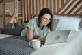 Young happy woman using laptop, typing, smiling and looking at screen, lying on bed at home Royalty Free Stock Photo