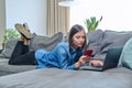 Young happy woman using smartphone laptop, lying on sofa at home Royalty Free Stock Photo