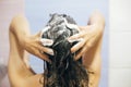 Young happy woman washing her hair with shampoo, hands with foam closeup. Back of beautiful brunette girl taking shower and Royalty Free Stock Photo