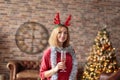 Young happy woman wearing red dress with antler deer headband holding champagne glass while smiling at camera. Royalty Free Stock Photo