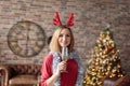 Young happy woman wearing red dress with antler deer headband holding champagne glass while smiling at camera.