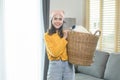 Young happy woman wearing yellow shirt holding a basket full of clothes at home, laundry concept