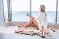 Young happy woman in a white knitted dress enjoying sea view next to big window with cup of tea. Panoramic window. Floor covering Royalty Free Stock Photo