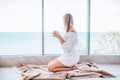 Young happy woman in a white knitted dress enjoying sea view next to big window with cup of tea. Panoramic window. Floor covering Royalty Free Stock Photo