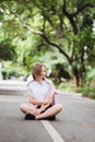 Young happy woman in white t-short is sitting in the middle of the asphalt road with greens on background