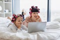 Woman lying with a cute girl on the bed, curling their hair, using a laptop. Royalty Free Stock Photo