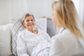 A health visitor talking to a sick senior woman lying in bed at home.
