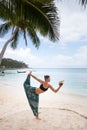 Beautiful young woman is doing yoga near the sea and drinks coconut