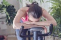 Young healthy fit woman training at home on exercise bike during work-out feeling exhausted and dizzy, lowered his head on his han Royalty Free Stock Photo