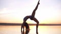 Young healthy fitness woman doing yoga, standing in bridge pose Setu Bandhasana on the seaside in the water at sunset