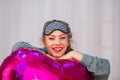 A young healthy girl in a sleep mask smiles and hugs a pink balloon in the shape of a heart