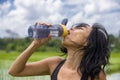 Young healthy sporty Asian Chinese woman drinking water bottle after fitness training and running workout outdoors on green field Royalty Free Stock Photo