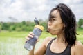 Young healthy sporty Asian Chinese woman drinking water bottle after fitness training and running workout outdoors on green field Royalty Free Stock Photo