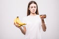Young healthy woman make a choise between bananas or donut on white background. Health concept Royalty Free Stock Photo