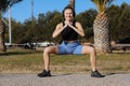 Young healthy woman in sportswear listens music in headphones while doing fitness squat leg exercises outdoors in park Royalty Free Stock Photo