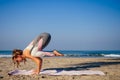Young healthy woman in a stylish one-piece jumpsuit practicing yoga on the beach at sunrise Royalty Free Stock Photo