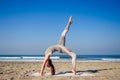 Young healthy woman in a stylish one-piece jumpsuit practicing yoga on the beach at sunrise Royalty Free Stock Photo