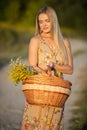A young herbalist stands on a sandy road with a basket full of herbs. Goldenrod and winter glory. She is facing the